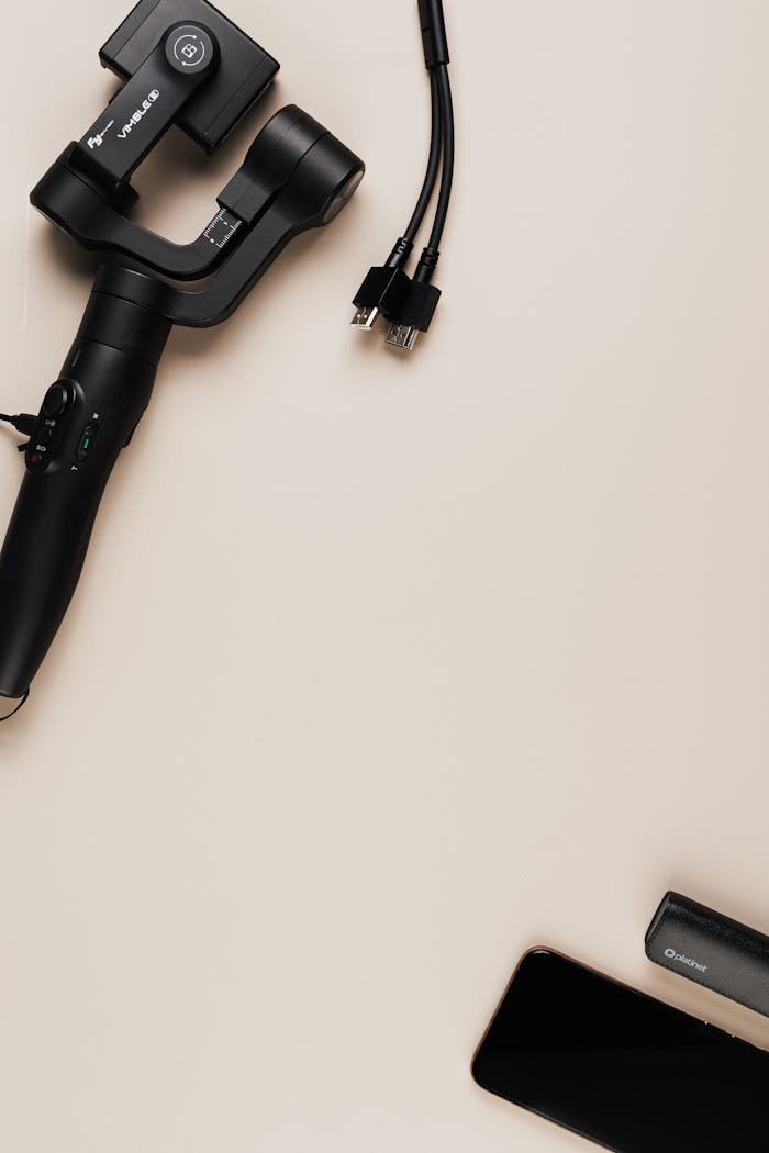 hero-img-01 Flat lay of a gimbal, smartphone, and cables on a neutral surface. Perfect for tech-related content.